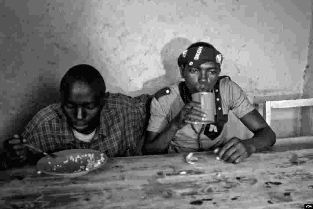 Vansing (right), drinks while he shares a meal with his friend Nshizirungu Amos, age 20. Vansing knew Nshizirungu Amos from an orphanage. Vansing says, &quot;Life in Giblioso is like jail, but we have to share.&quot; (Hamada Elrasam for VOA)