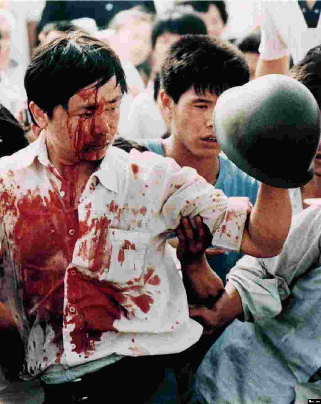 一名满身是血的抗议者手举一顶中国士兵的头盔。在天安门民主运动期间，抗议者与中国军队发生了暴力冲突。（1989年6月4日）