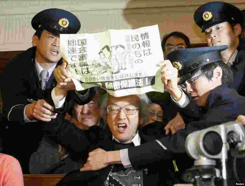 A spectator holds a sign against a government proposed state secrecy act as parliamentary security officers try to stop him during a lower house special committee meeting on the act at the parliament in Tokyo, Japan, in this photo taken by Kyodo.