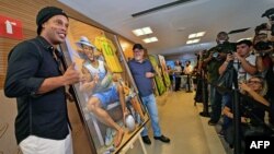 Mantan bintang sepak bola, Ronaldinho (kiri) melihat sebuah lukisan oleh seniman Emerson Carvalho de Souza (tengah), dalam foto bersama di sebuah acara di Stadion Maracana, Rio de Janeiro, Brasil, 28 Februari 2019.
