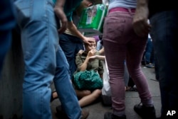 Irama Carrero is aided by fellow shoppers after fainting in a food line outside a grocery store, in the afternoon in Caracas, Venezuela, May 5, 2016.
