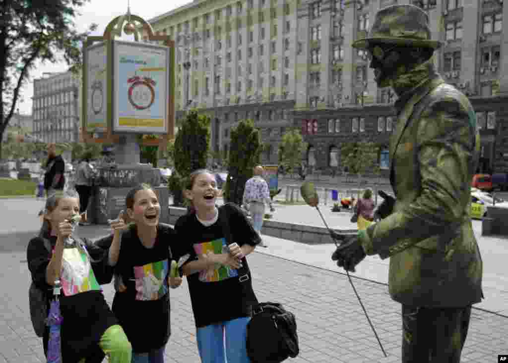 Tiga remaja puteri bereaksi terhadap seniman jalanan di kota Kyiv, Ukraina.