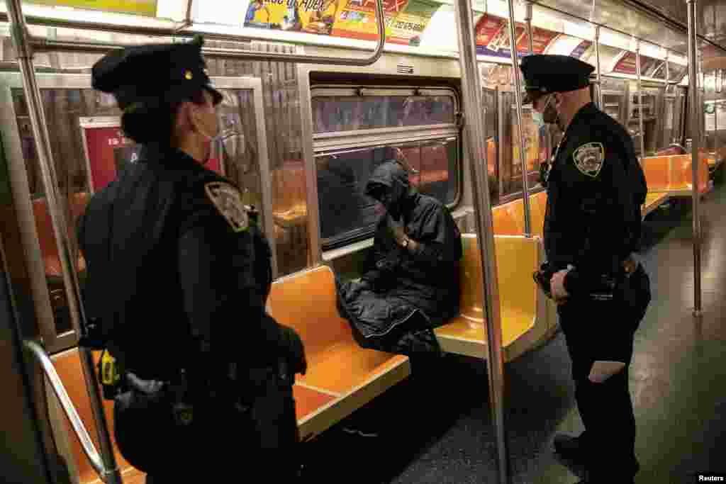 New York City Police (NYPD) officers wake up a passenger on a subway train.