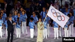 FILE - Tokyo governor Yuriko Koike waves the Olympic flag as International Olympic Committee (IOC) President Thomas Bach applauds at the closing ceremony of the 2016 Rio Olympics in Rio de Janeiro, Brazil, Aug. 21, 2016.