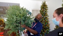 FILE - Balsam Hill Outlet manager Kelly Bratt, right, helps sales associate Rickey Haynes set up a tree during job training in Allen, Texas, Sept. 20, 2021. Businesses are grappling with increasing demands from hourly workers for more flexible schedules and other benefits.