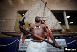 A traditionally dressed Fijian warrior with a weapon poses for a picture in front of a Fijian double-hulled sailing canoe during the COP23 U.N. Climate Change Conference 2017, hosted by Fiji but held in Bonn, at World Conference Center Bonn, Germany, Nov. 6, 2017.