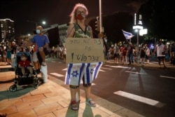 An Israeli protester holds a banner saying, "It's not a lockdown, it's a political curfew," during a demonstration against lockdown measures, in Tel Aviv, Israel, Oct. 3, 2020.