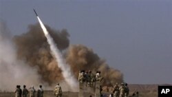 In this photo released by the semi-official Iranian Mehr News Agency, Iranian revolutionary Guards personnel, foreground, watch the launch of a Zelzal missile during military maneuvers outside the city of Qom, Iran, June 28, 2011