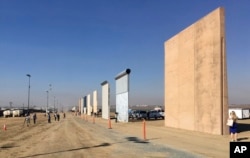 FILE - People look at prototypes of a border wall, Oct. 26, 2017, in San Diego, California. Construction of a wall between the U.S. and Mexico, a key campaign promise, remains high on President Donald Trump's agenda.
