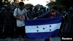Migrantes hondureños que intentan llegar a Estados Unidos sostienen una bandera nacional mientras están parados frente a soldados guatemaltecos que bloquean la carretera para evitar que lleguen a México, el 2 de octubre 2020. 