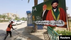 A worker cleans the street next to a campaign poster of candidates ahead of the parliamentary election, in Najaf, Iraq, April 14, 2018.