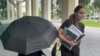 La famosa diseñadora de bolsos Nancy González se esconde bajo un paraguas mientras camina con su abogada Andrea López afuera del tribunal federal en Miami el lunes 22 de abril de 2024. 