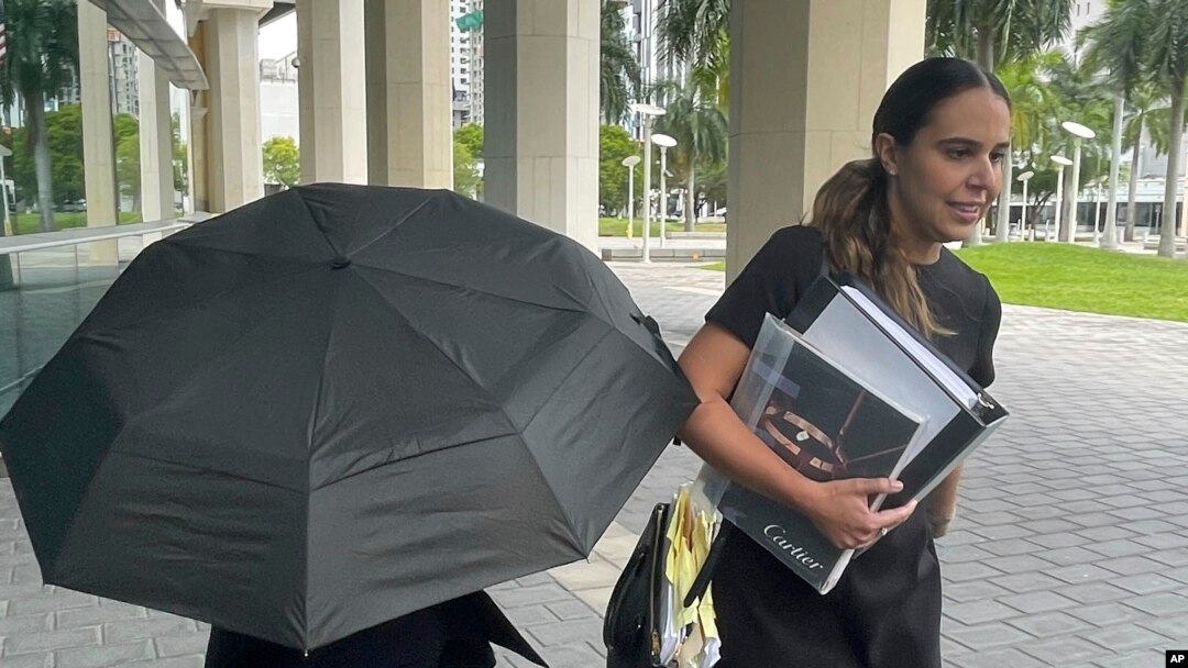La famosa diseñadora de bolsos Nancy González se esconde bajo un paraguas mientras camina con su abogada Andrea López afuera del tribunal federal en Miami el lunes 22 de abril de 2024. 