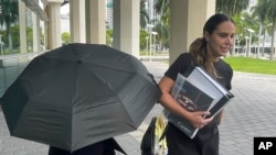 La famosa diseñadora de bolsos Nancy González se esconde bajo un paraguas mientras camina con su abogada Andrea López afuera del tribunal federal en Miami el lunes 22 de abril de 2024. 