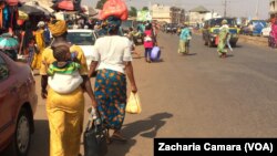 Des femmes quittant un marché de la banlieue de Conakry avec des sacs plastiques, en Guinée, le 17 janvier 2018. (VOA/Zacharia Camara)