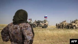 (File) A Syrian woman looks at US and Russian soldiers in the northeastern Syrian town of al-Malikiyah (Derik) at the border with Turkey, June 3, 2020.