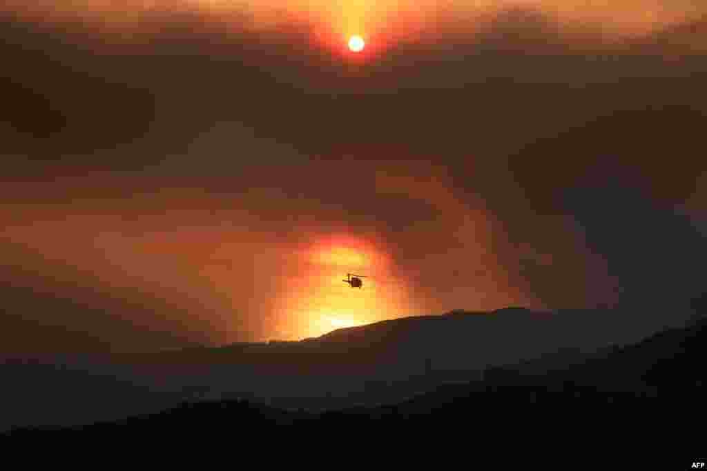 A helicopter drops water as a mountainside burns while the Franklin Fire grows in Malibu, California, Dec. 10, 2024.