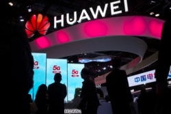 FILE - In this Oct. 31, 2019, file photo, attendees walk past a display for 5G services from Chinese technology firm Huawei at the PT Expo in Beijing.