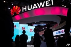 FILE - In this Oct. 31, 2019, file photo, attendees walk past a display for 5G services from Chinese technology firm Huawei at the PT Expo in Beijing.
