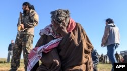 A member of the Kurdish-led Syrian Democratic Forces (SDF) stands by, left, as a man sits with his head in his hand, after leaving the Islamic State (IS) group's last holdout of Baghuz, in the eastern Syria, March 1, 2019.