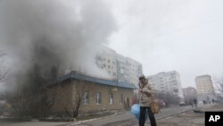 Seorang perempuan melewati rumah yang terbakar akibat serangan roket di Mariupol, Ukraina timur (24/1). (AP/Sergey Vaganov)