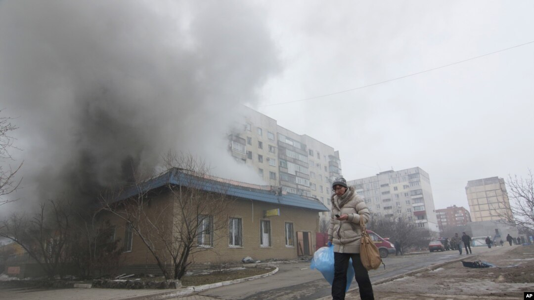Seorang perempuan melewati rumah yang terbakar akibat serangan roket di Mariupol, Ukraina timur (24/1). (AP/Sergey Vaganov)