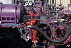 FILE - A worker adjusts hoses during a hydraulic fracturing operation at an Encana Corp. oil well, near Mead, Colorado, on March 25, 2014.