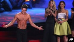 Zac Efron acepta el premio a la mejor actuación sin camisa. Atrás, observan Rita Ora and Jessica Alba.