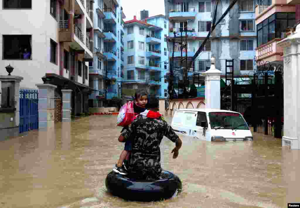 A member of Nepalese army carrying a child walks along the flooded colony in Kathmandu, Nepal.