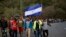 Honduran migrants walk north along a road in hopes of reaching the United States, one carrying a Honduran flag, as they leave Esquipulas, Guatemala, just after sunrise, Jan. 17, 2020.