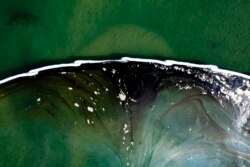 An aerial photo shows floating barriers known as booms set up to try to stop further incursion into the Wetlands Talbert Marsh after an oil spill on Huntington Beach, Calif., Oct. 4, 2021.