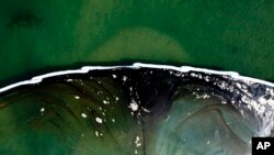 საჰაერო კამერით გადაღებული ფოტო, რომელიც მოტივტივე ბარიერებით გაჟონილი ნავთობის სანაპიროსკენ გავრცელების შეჩერებას ცდილობს. 4 ოქტომბერი, 2021 (AP Photo/Ringo H.W. Chiu)