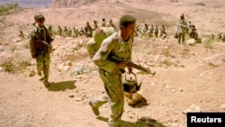 FILE - An Eritrean soldier carries his rifle and teapot as the Eritrean army begins to pull out from the frontline near Senafe, Feb. 17, 2001. 