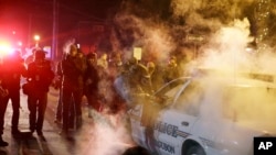 A police officer approaches a police vehicle after a protester has thrown a smoke device from the crowd Tuesday, Ferguson, Mo., Nov. 25, 2014