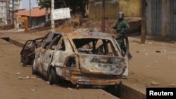 A security officer walks past a burned car in Conakry, Guinea, where youths clashed with security forces, raising pressure on President Alpha Conde ahead of talks with the opposition on a dispute over the timing of elections, May 7, 2015. 
