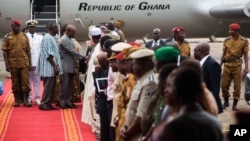 Le président du Ghana John Dramani Mahama, arrière centre, serrant la main des personnes venues l’accueillir à l'aéroport de Ouagadougou, au Burkina Faso, le mercredi 5 novembre 2014, avec à ses côtés le lieutenant-colonel Isaac Yacouba Zida, arrière gauche. (AP Photo / Theo Renaut)
