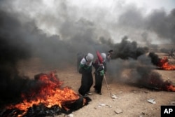 Two women hold Palestinian flags as they walk through burning tires during a protest at the Gaza Strip's border with Israel, May 4, 2018.