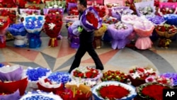 A man carries a bouquet of Valentine's Day roses as he walks past other flower arrangements for sale at the flower market in Beijing, Feb. 14, 2017.