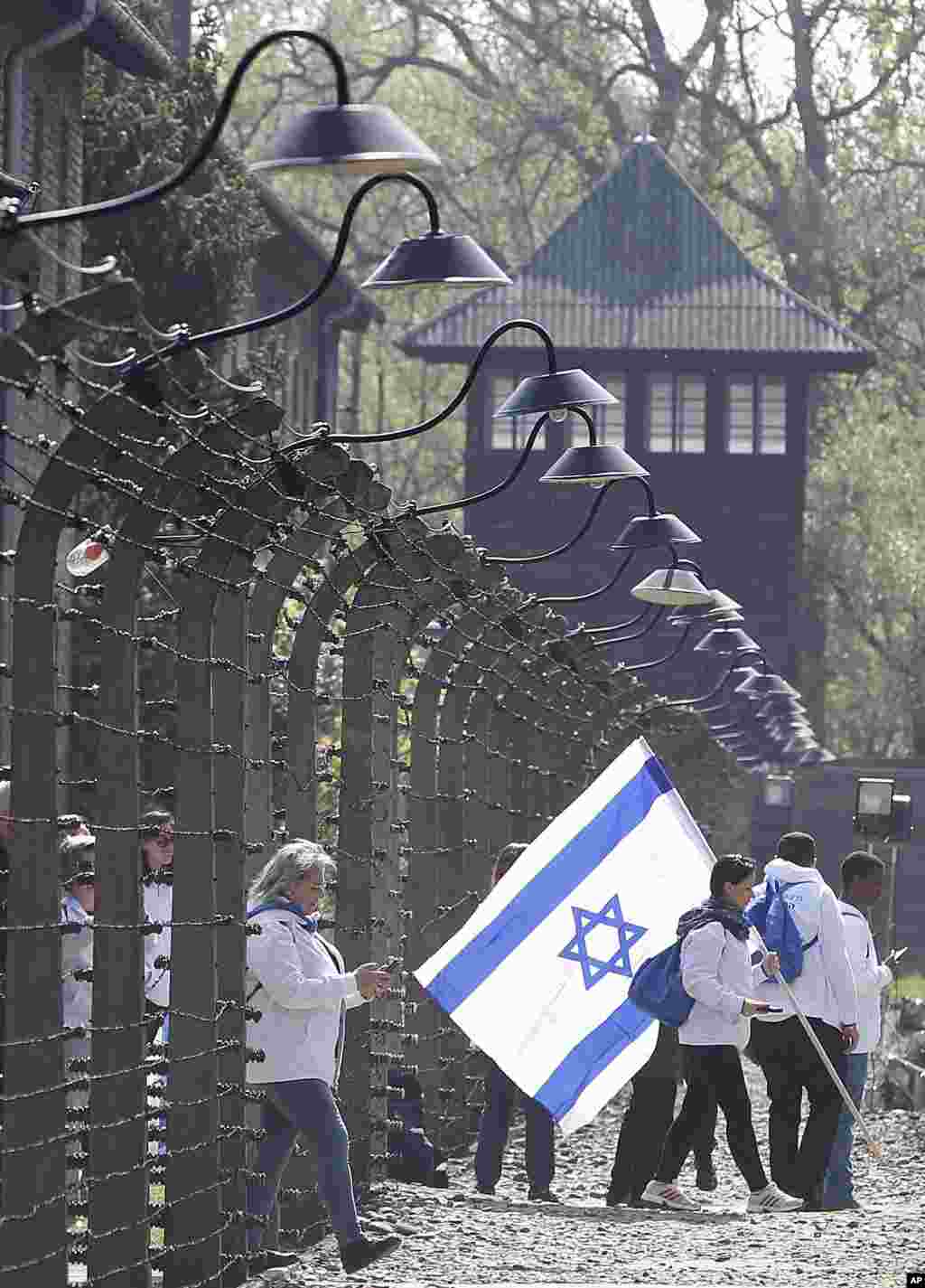 یک گروه از بازدید کنندگان با پرچم اسرائیل در اردوگاه &laquo;آشویتس&raquo; در دوران آلمان نازی که اکنون در لهستان قرار دارد. هولوکاست یادآور نسل کشی یهودیان است که نازی&zwnj;ها دست کم شش میلیون یهودی را کشتند.