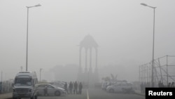 FILE - Vendors selling drinks stand beside vehicles near the India Gate war memorial on a smoggy day in New Delhi, Feb. 1, 2013. 