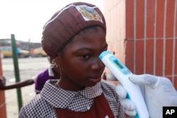 A teacher uses a thermometer to test students' temperature checking for signs of Ebola virus at Aiyetoro African Church Nursery and Primary school in Lagos, Nigeria on Oct. 8, 2014.
