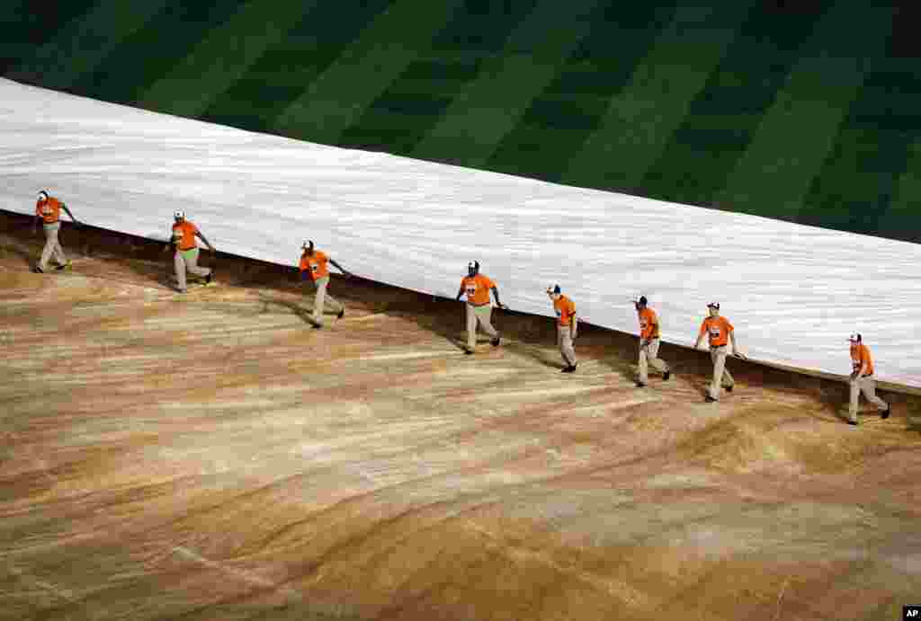 Groundskeepers remove a tarp from the field during a rain delay between the first and second baseball games of a doubleheader between the Baltimore Orioles and the Pittsburgh Pirates, Thursday, May 1, 2014, in Maryland.