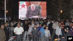 People congregate around a large TV screen showing Algeria's President Abdelaziz Bouteflika in Algiers, April 15, 2011