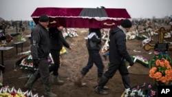 Ukrainian municipal workers carry a coffin bearing the body of one of 30 civilians killed during shelling by suspected pro-Russian separatists of Mariupol, Ukraine, on Jan. 27, 2015. 