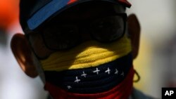 Un manifestante, con una mascarilla tejida a mano con los colores representativos de la bandera venezolana, asiste a una marcha exigiendo una distribución más equitativa y rápida de las vacunas contra el COVID-19 en Caracas, el 7 de abril de 2021.