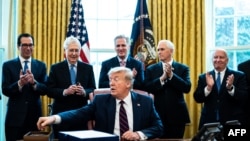 Treasury Secretary Steven Mnuchin, left, Vice President Mike Pence, second from right, and Republican lawmakers applaud President Donald Trump during a signing ceremony for H.R. 748, the CARES Act, at the White House, March 27, 2020.
