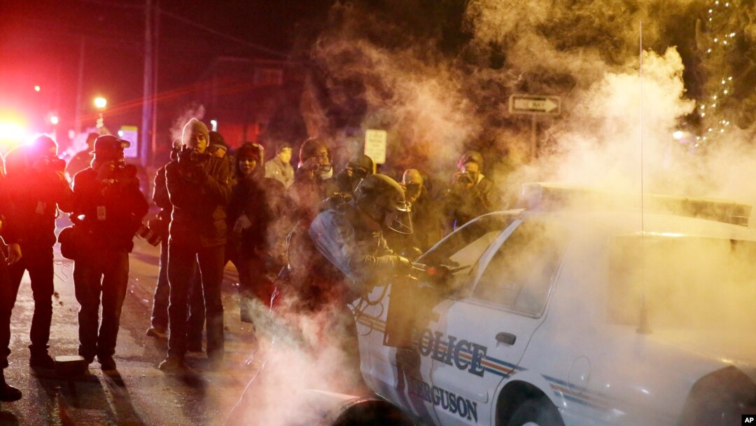 Polisi mendekati mobil polisi setelah seorang demonstran melemparkan alat berasap di Ferguson, Missouri (25/11). (AP/David Goldman)