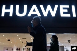 FILE - Residents pass by a Huawei electronics store in Beijing, April 12, 2021.