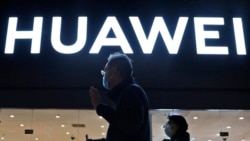 FILE - Residents pass by a Huawei electronics store in Beijing, April 12, 2021.