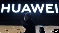 FILE - Residents pass by a Huawei electronics store in Beijing, April 12, 2021. 